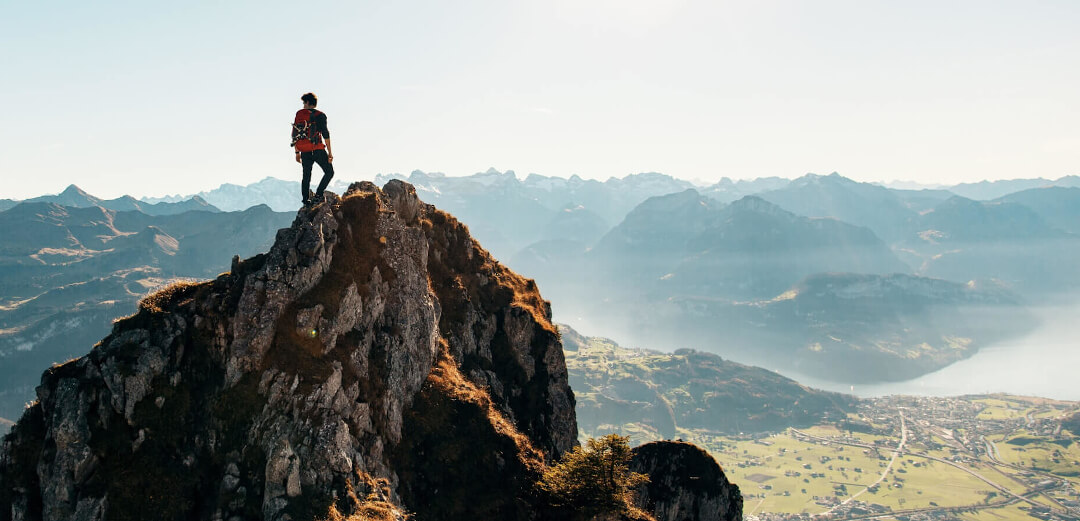 EIn Mann steht auf einem Berggipfel und schau sich um